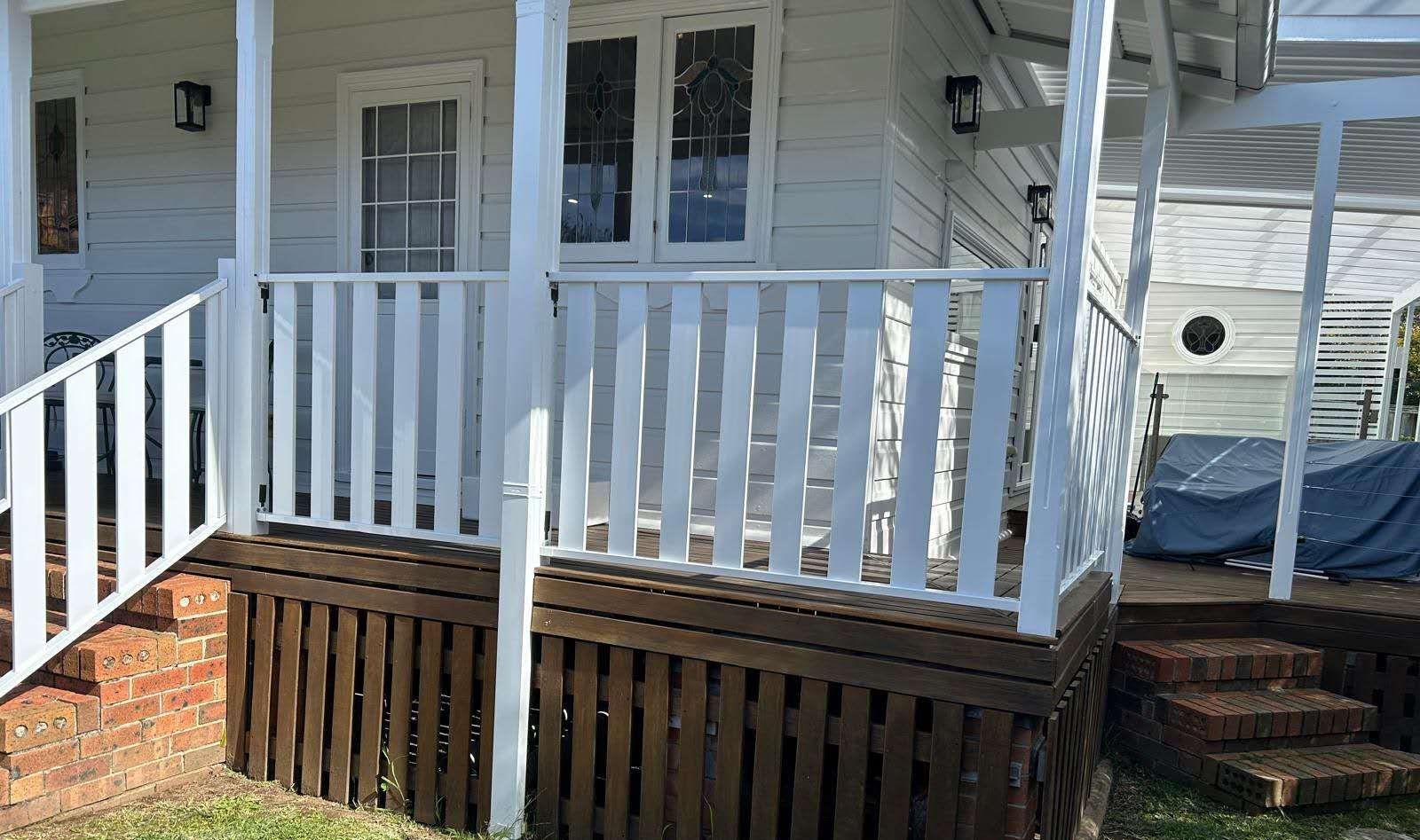 White porch railing and white support posts installed on a wooden deck in front .