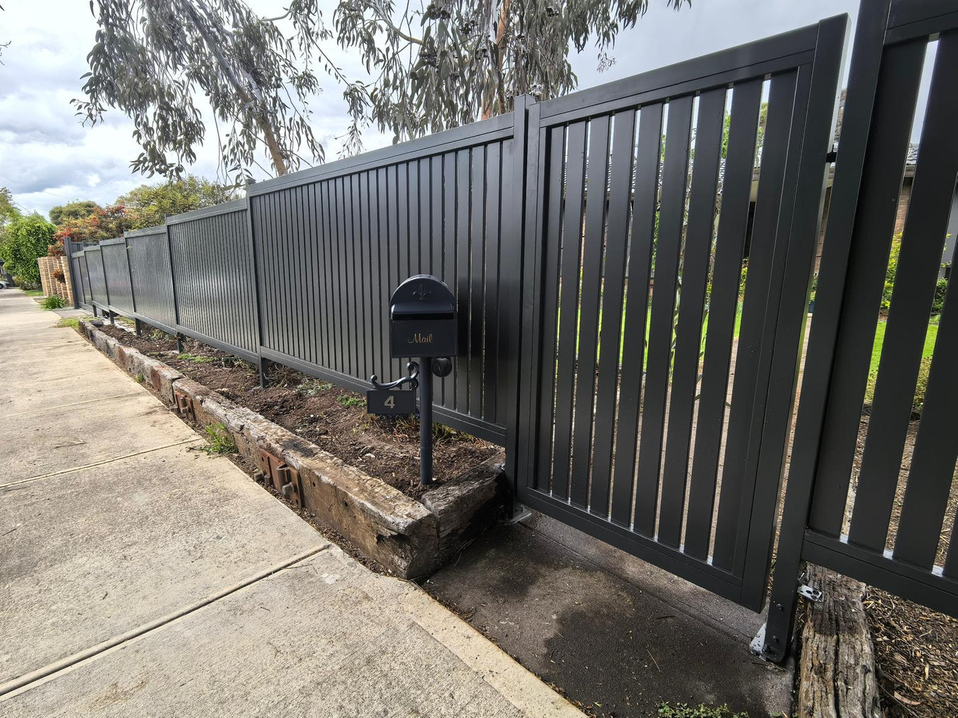 Black metal fence with a gate and mailbox on a residential street.