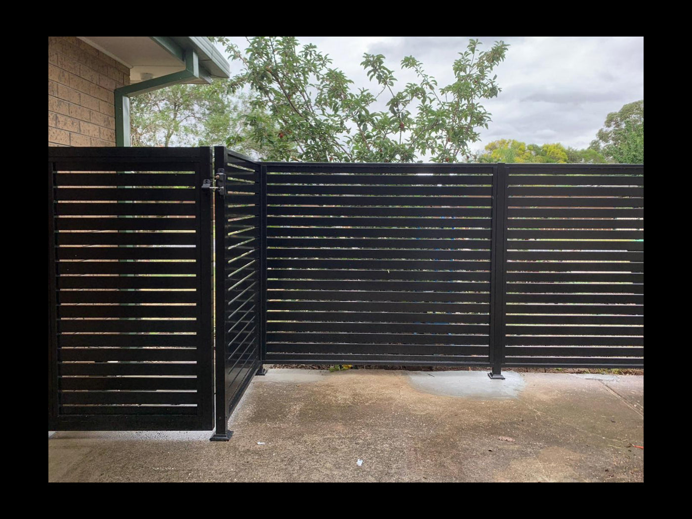Black metal gate with horizontal slats in front of a house